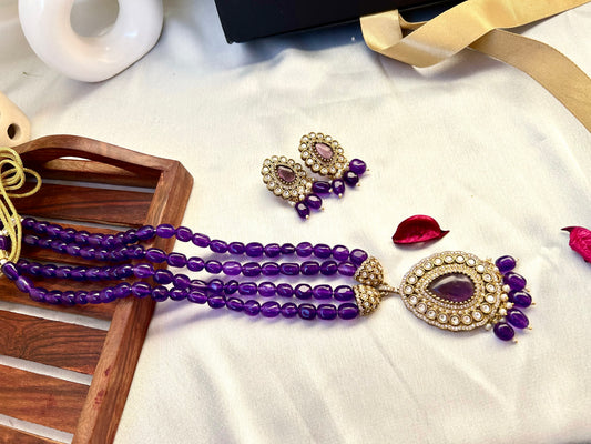 Parineeti purple Kundan Rani Haar – A gold-plated Rani Haar necklace with purple gemstones and matching earrings, set on a rustic wooden backdrop."